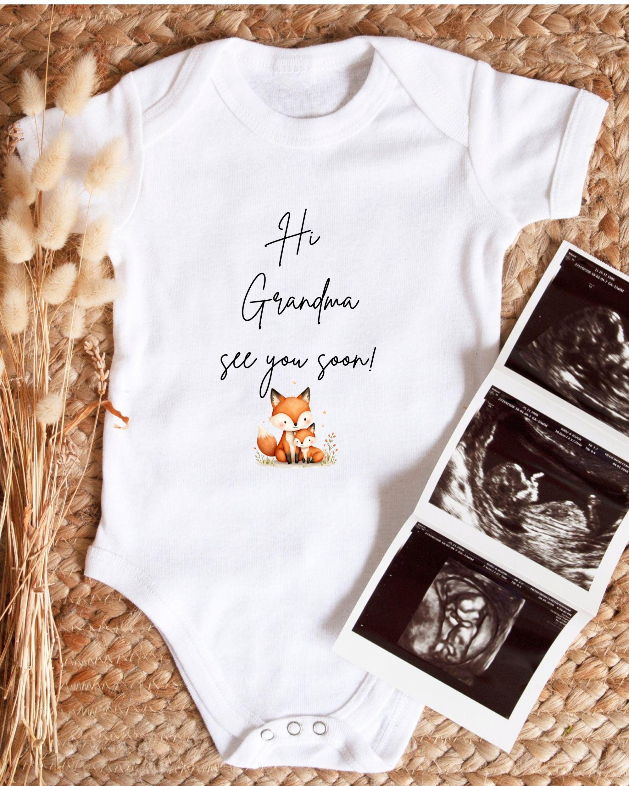 A white baby onesie with a fox graphic and the text "Hi Grandma, see you soon!" is displayed alongside a set of three black and white ultrasound images.