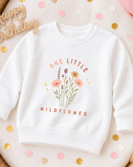 A white sweatshirt with a floral design and the text "One Little Wildflower" printed on it, surrounded by confetti.