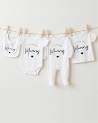 A row of four white baby clothes with the text "I love my Mummy" printed on them, hanging on a clothesline.