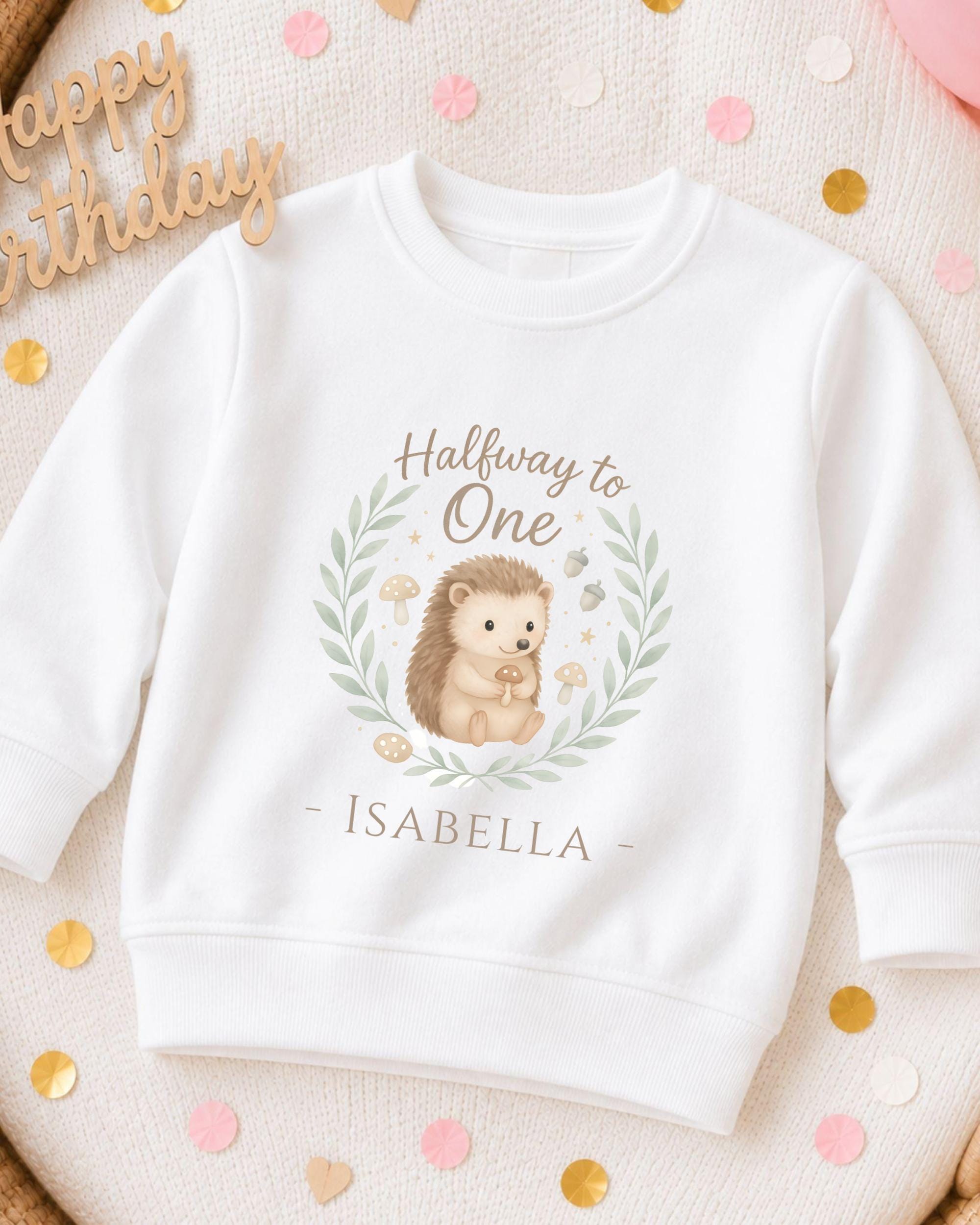 A white sweatshirt with a hedgehog graphic and the text "Halfway to One - Isabella" printed on it, surrounded by confetti.