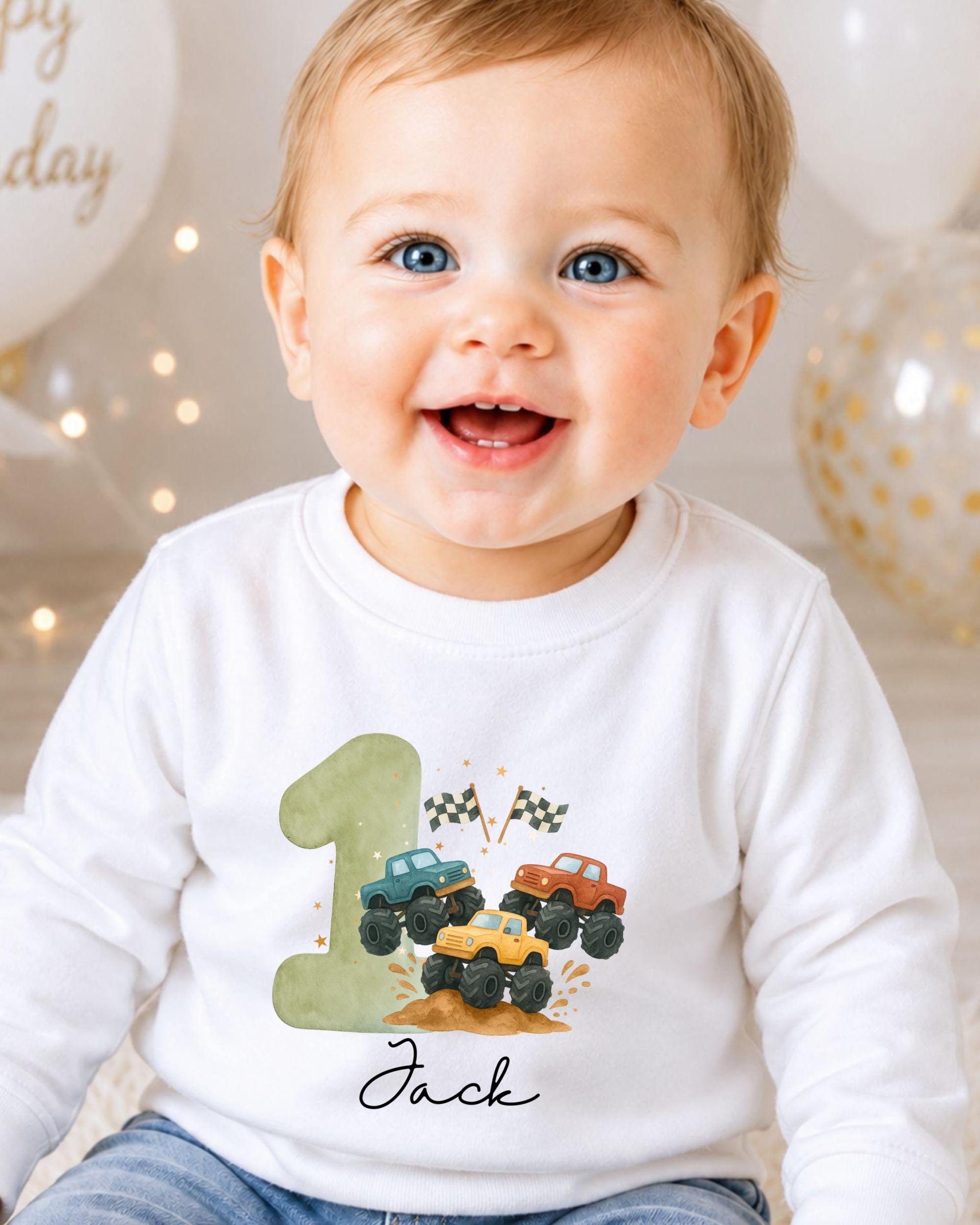 A smiling baby boy wearing a white shirt with a graphic of a truck and the number 1, surrounded by colorful balloons.