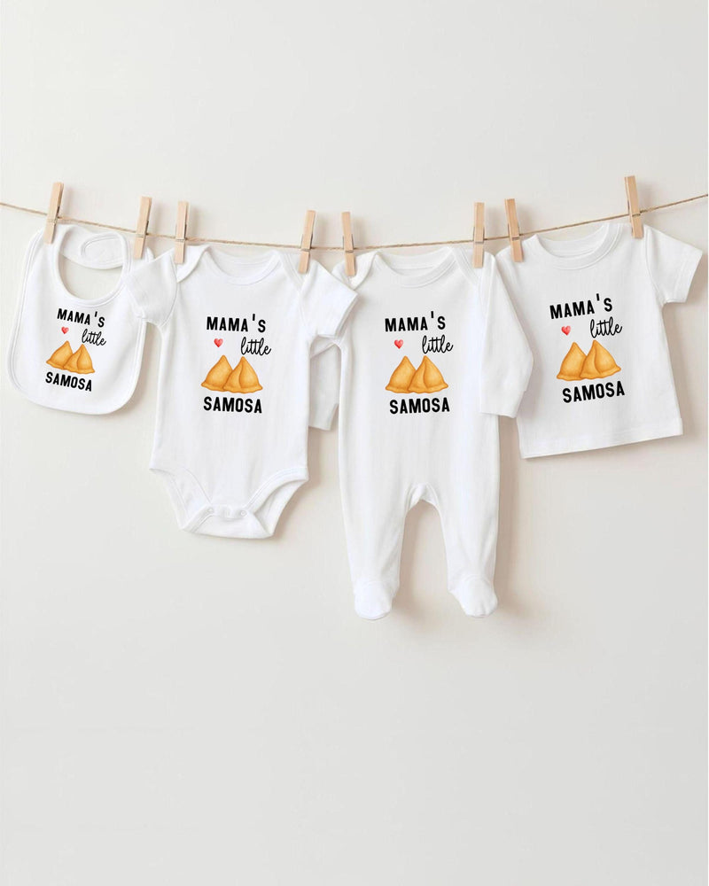 A row of four white baby clothes with the text "MAMA'S LITTLE SAMOSA" printed on them, hanging on a clothesline.