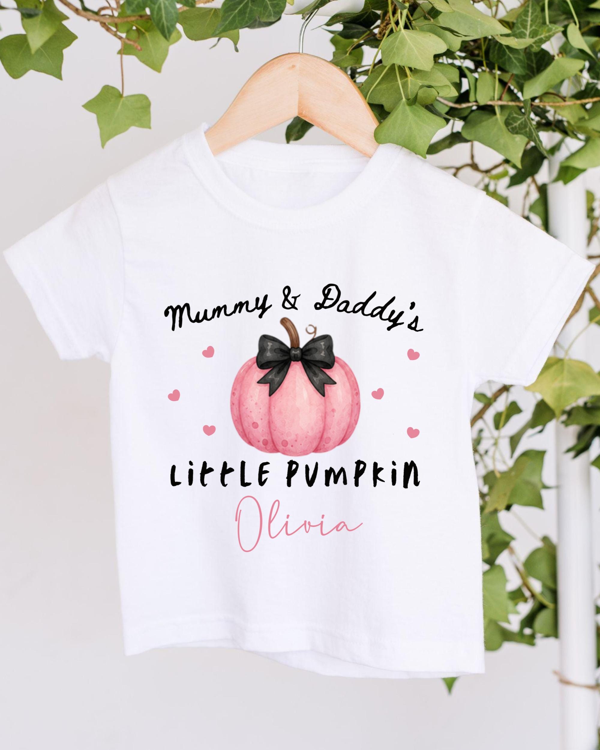 A white t-shirt with a graphic design featuring a pink pumpkin and the text "Mummy & Daddy's LITTLE PUMPKIN Olivia" printed on it.