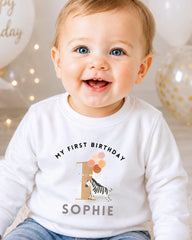 A smiling baby wearing a white shirt with a birthday message and a graphic of a zebra.