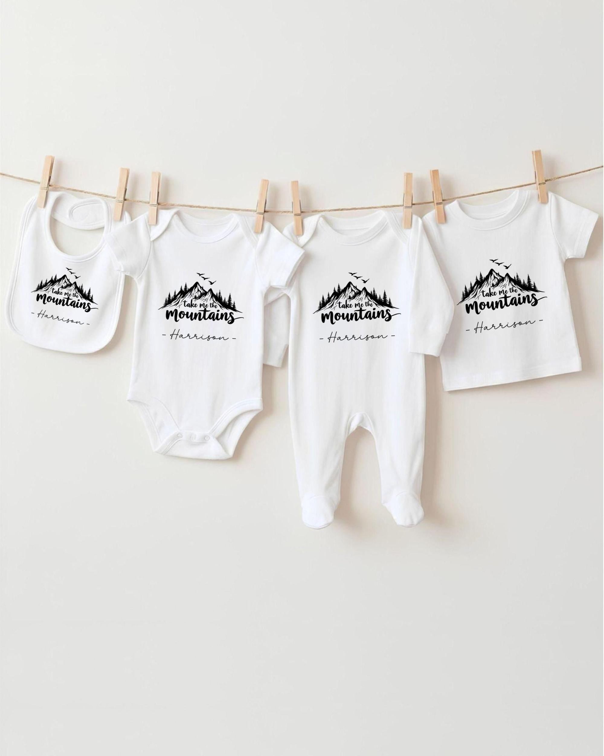 A row of four white baby clothes with a mountain design, hanging on a clothesline.