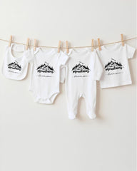 A row of four white baby clothes with a mountain design, hanging on a clothesline.
