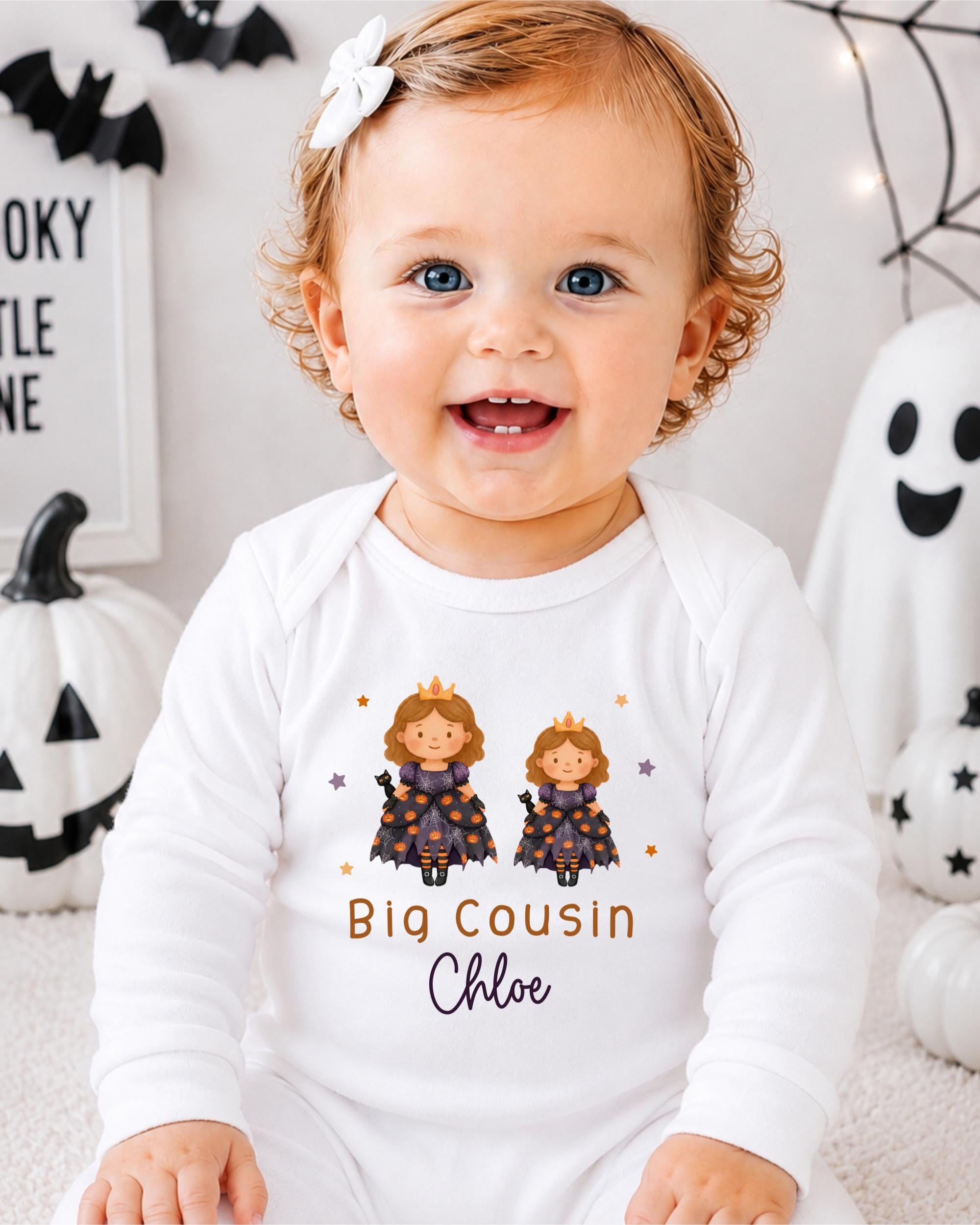 A smiling baby girl wearing a white onesie with a Halloween-themed design, including two cartoon princesses and the text "Big Cousin Chloe".