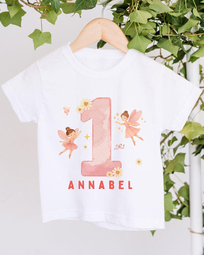 A white t-shirt with a pink number one and two-tailed fairy design, along with the text "Annabel" printed on it.