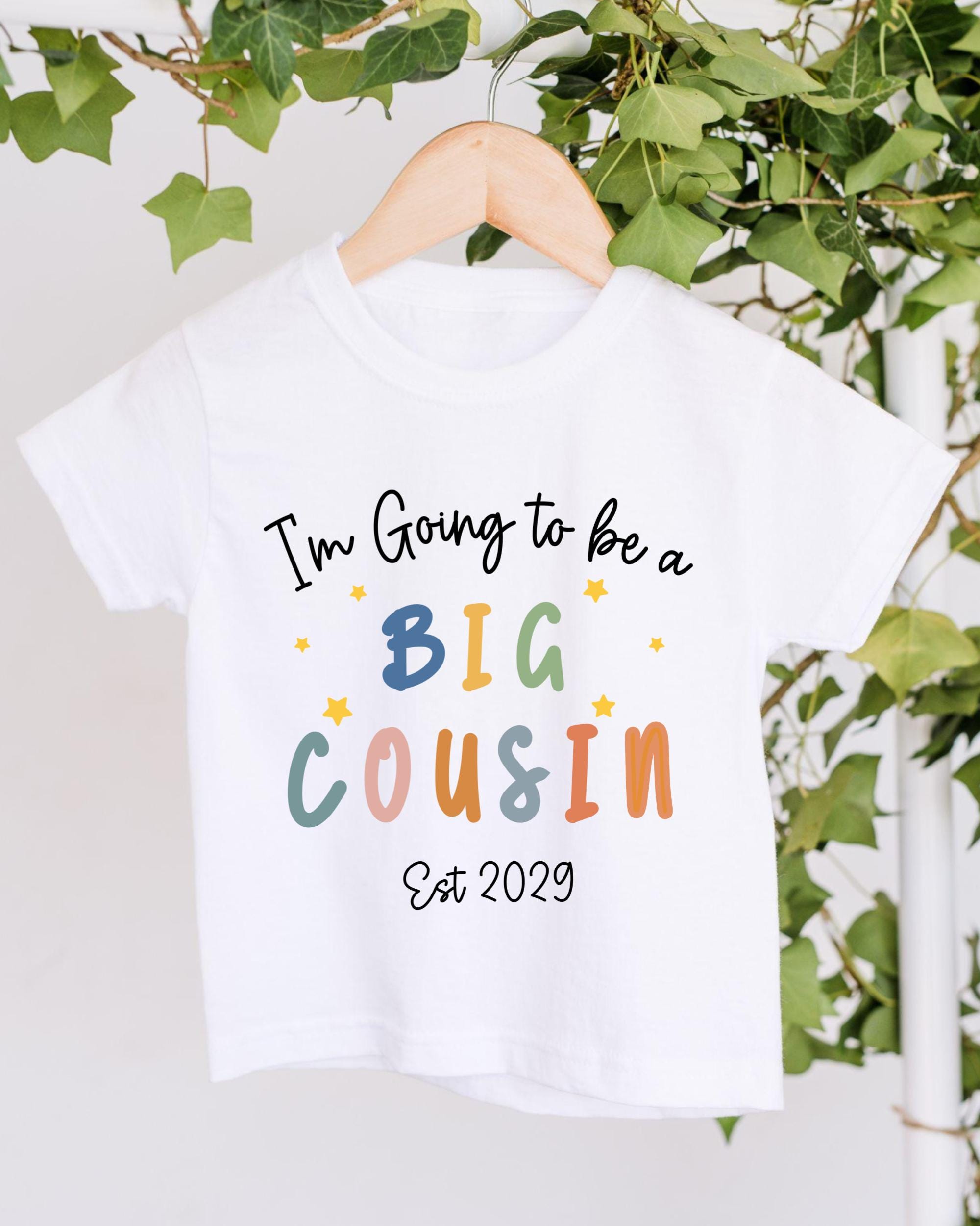 A white t-shirt with text that says "I'm Going to be a Big Cousin" and "Est 2029" printed on it.