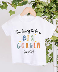 A white t-shirt with text that says "I'm Going to be a Big Cousin" and "Est 2029" printed on it.