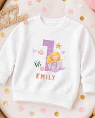 A white sweatshirt with a mermaid character and the number 1 printed on it, along with the name "EMILY" below the number.