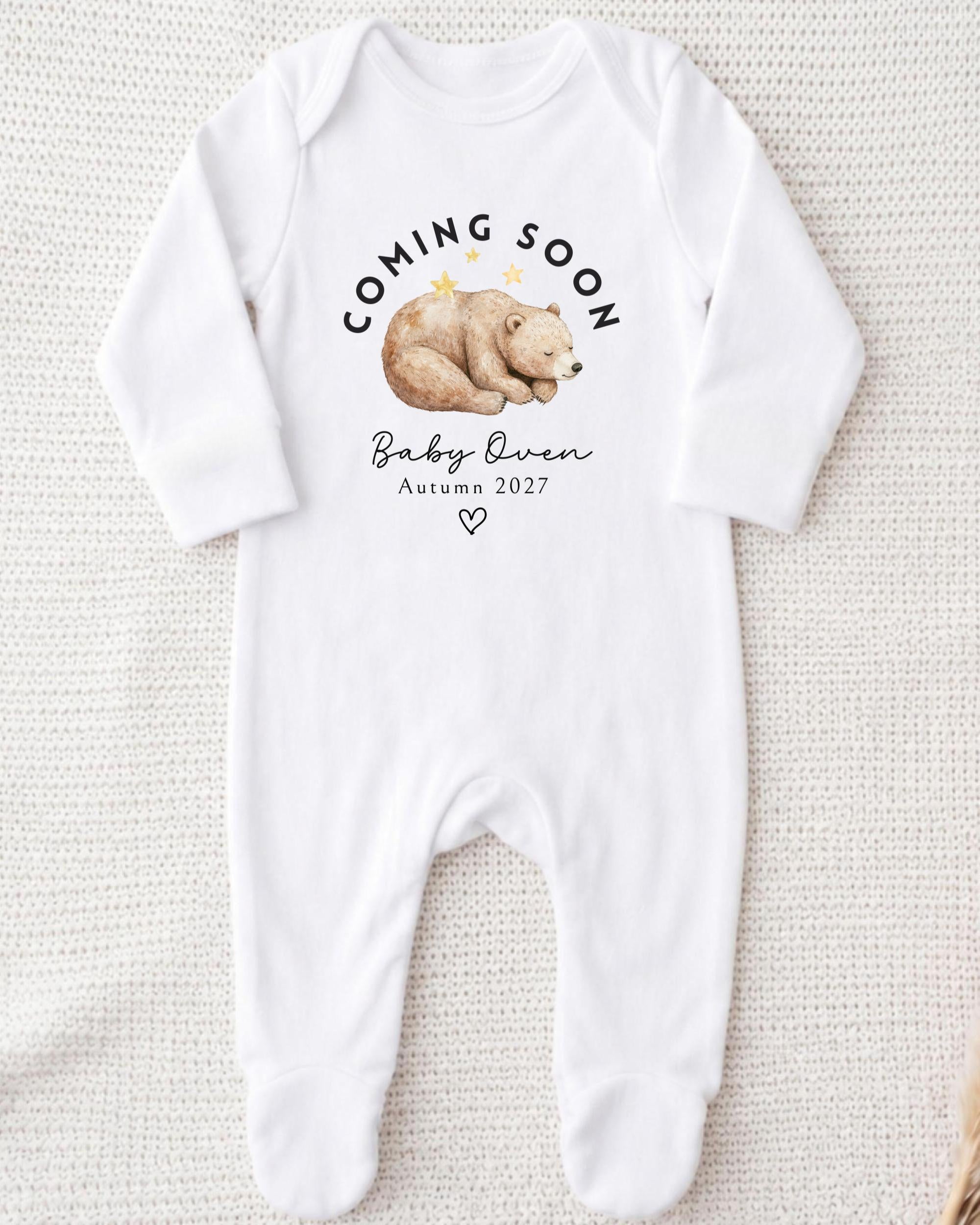 A white onesie with a graphic of a sleeping bear and text that says "Coming soon Baby Queen Autumn 2027".