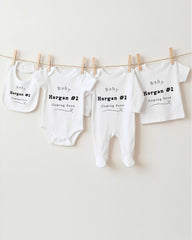 four white baby clothes hanging on a clothesline, each with a unique name printed on it.
