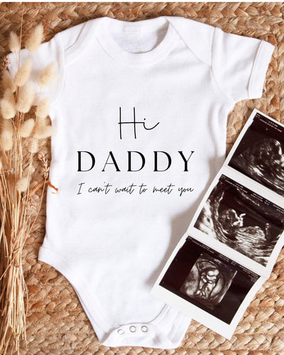 White Baby Vest with black 'Hi Daddy I can't wait to meet you' lettering in fine script and large serif capitals for a pregnancy announcement.