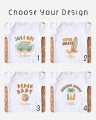 four different designs of white baby shirts, each featuring a unique beach-themed graphic. The designs include a surfboard, a beach ball, a palm tree, and a surfer.