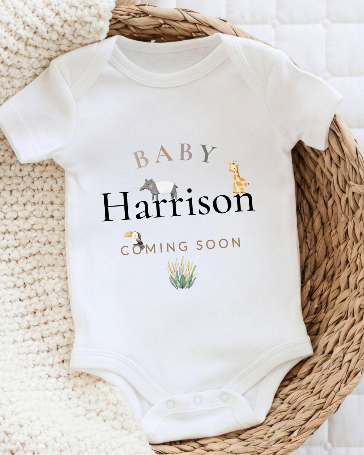 A white baby onesie with the text "BABY Harison COMING SOON" printed on it, along with illustrations of various animals.