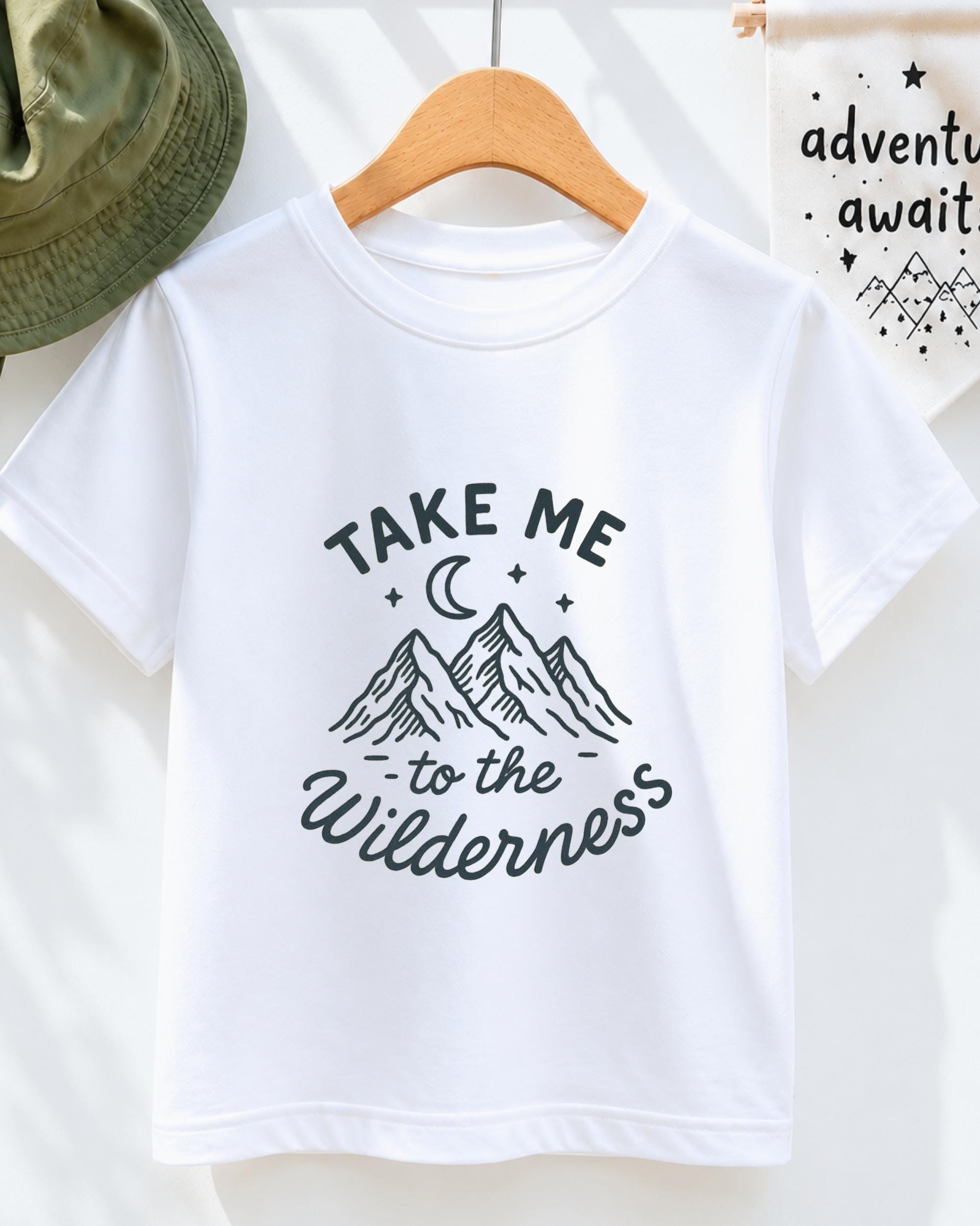 A white t-shirt with a graphic design of mountains and a crescent moon, along with the text "Take me to the Wilderness" printed on it.