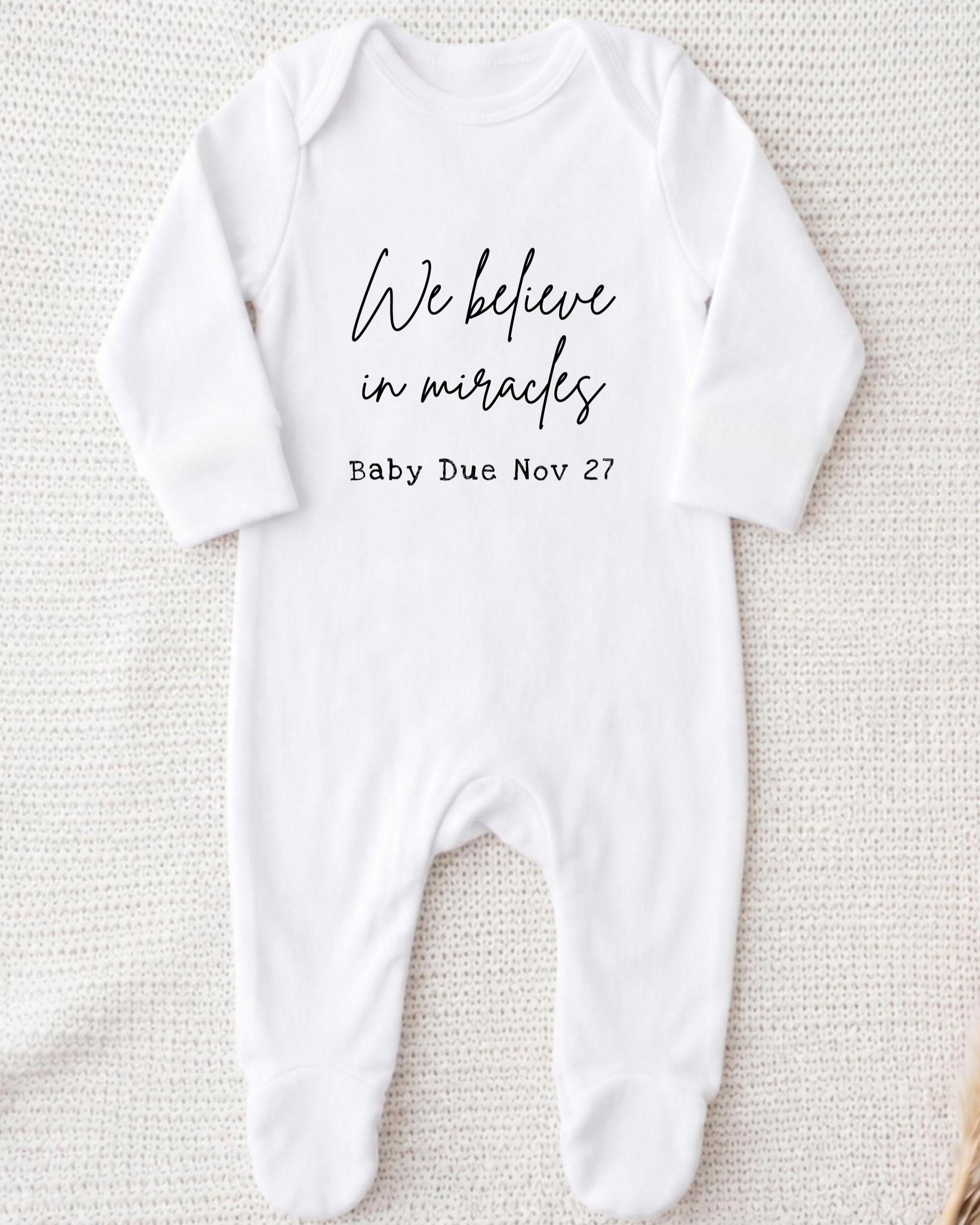 A white onesie with the text "We believe in miracles" printed on it, along with the date "Baby Due Nov 27".
