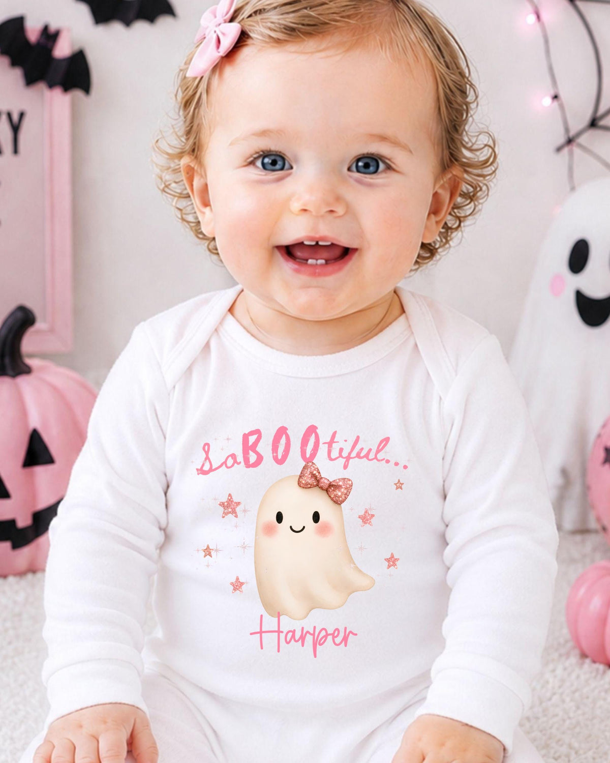 A smiling baby girl wearing a white onesie with a ghost and the text "So BOO TIFUL Harper" printed on it.