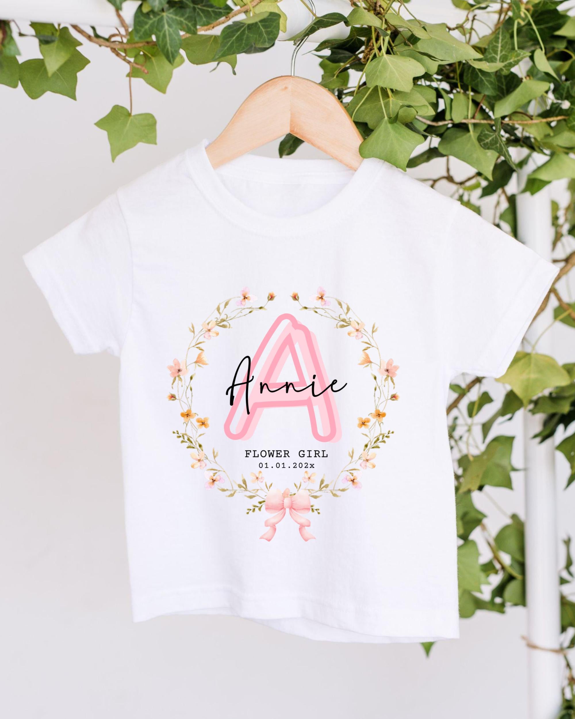 A white t-shirt with a floral design and the name "Annie" printed on it, hanging on a wooden hanger.