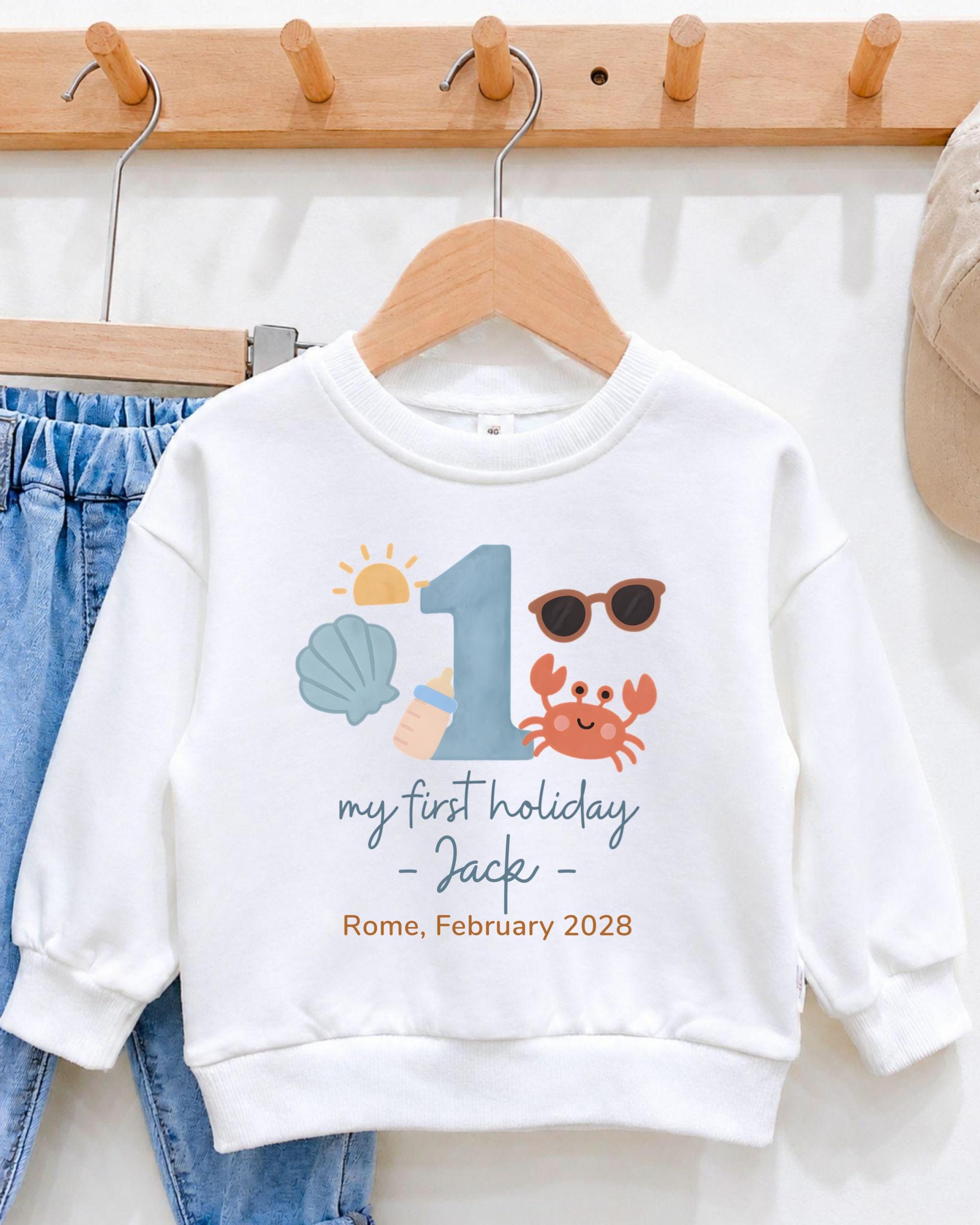 A white sweatshirt with a graphic design featuring a sun, sunglasses, a crab, and the text "my first holiday - Jack - Rome, February 2008".