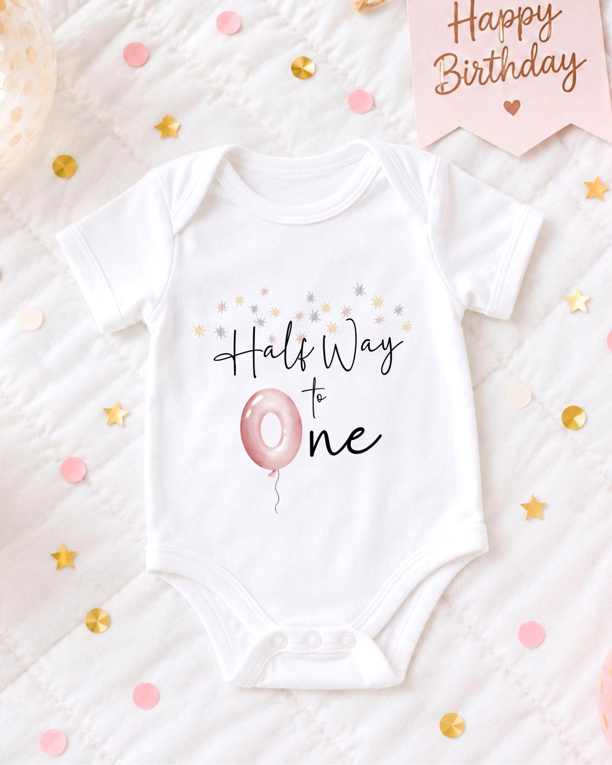 A white onesie with the text "Hals Way to One" printed on it, along with a pink balloon and confetti.