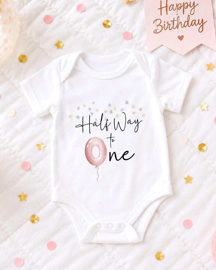 A white onesie with the text "Hals Way to One" printed on it, along with a pink balloon and confetti.
