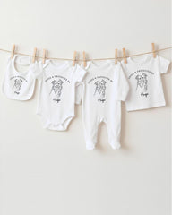 A row of white baby clothes, including onesies and bibs, hanging on a clothesline.