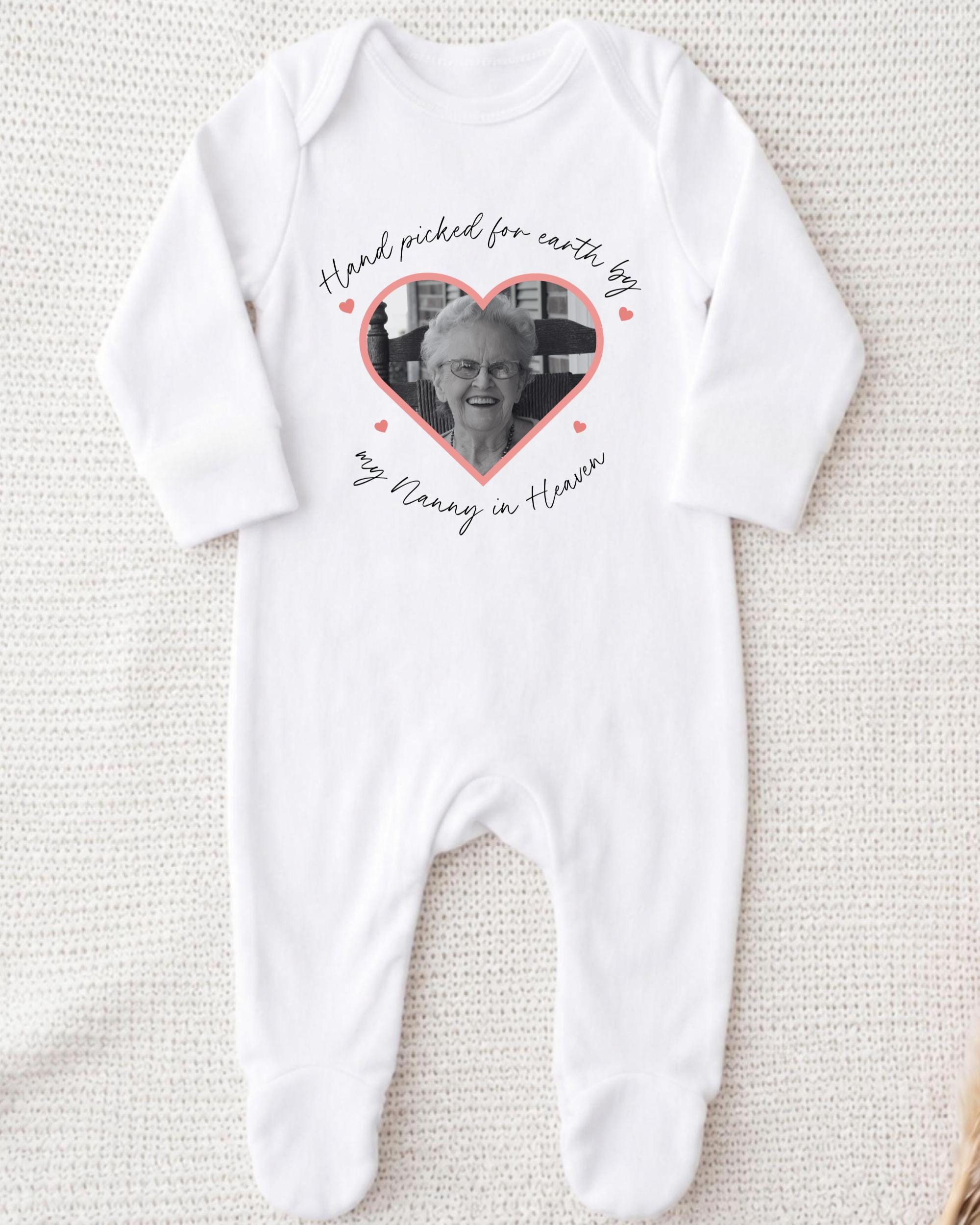 A white onesie with a heart-shaped photo of an elderly woman printed on it, along with the text "Hand picked for earth by my Nanny in heaven".