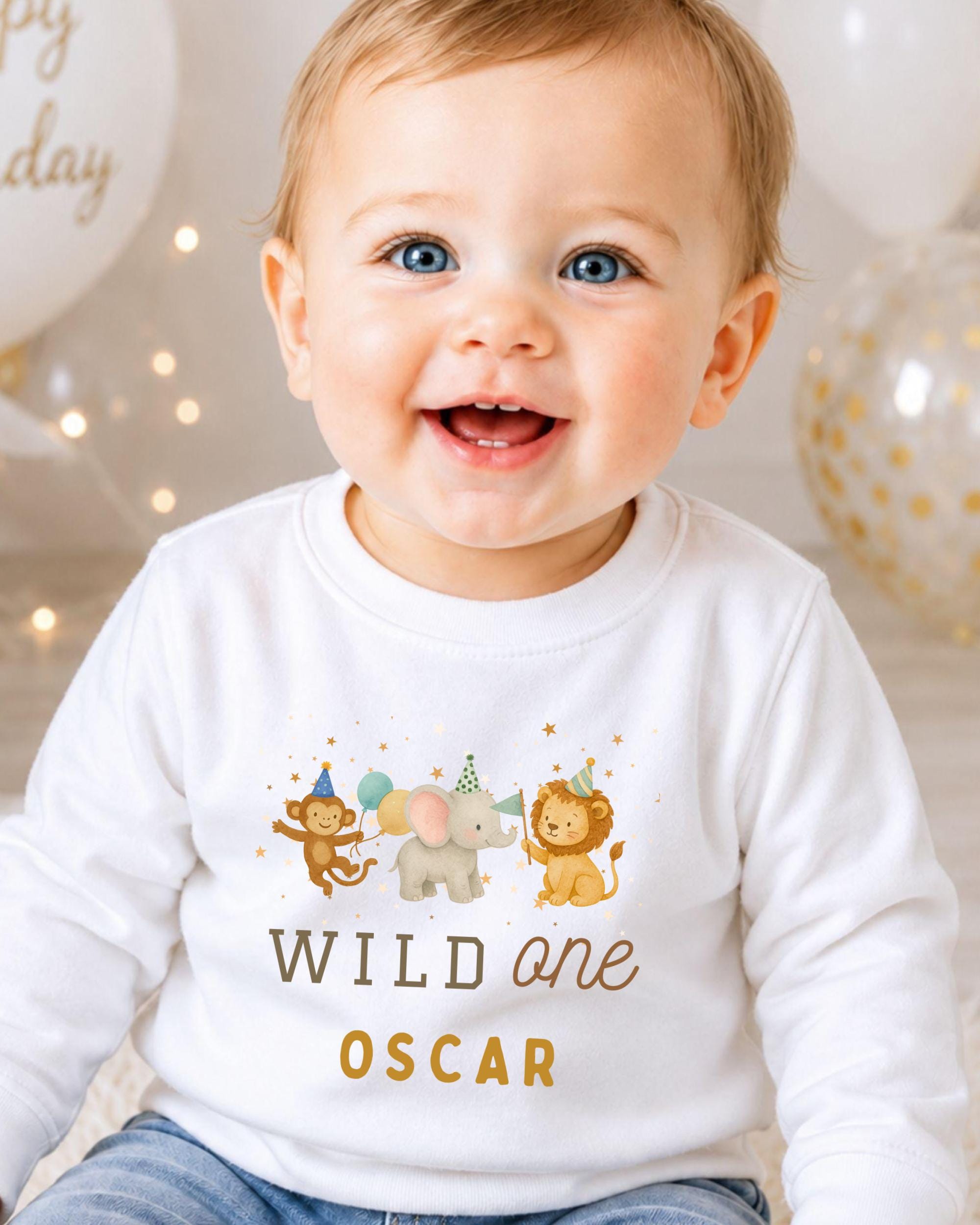 A smiling baby boy wearing a white shirt with a cartoon animal design and the text "WILD one OSCAR" printed on it.