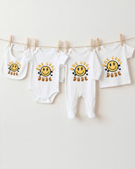A collection of baby clothes, including onesies and bibs, hanging on a clothesline.