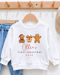 A white sweatshirt with a personalized design featuring a gingerbread man, a reindeer, and a teddy bear, along with the text "Ollie's first Christmas 2006".