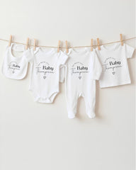 a collection of white baby clothes hanging on a clothesline, each with a personalized name printed on it.