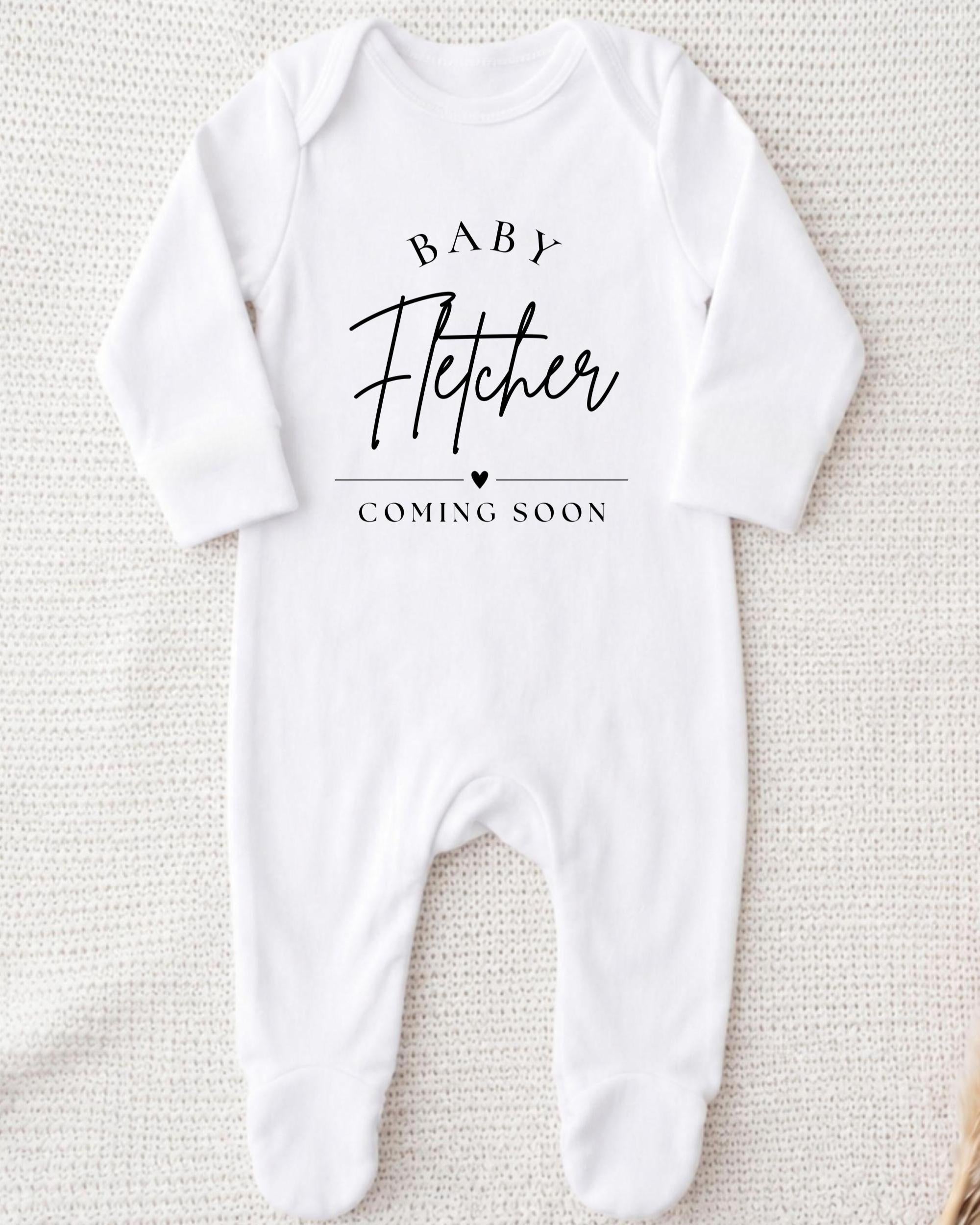 A white onesie with the text "BABY FETCHER COMING SOON" printed on it.