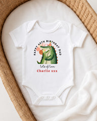 A white onesie with a cartoon alligator and text on it, placed in a woven basket.