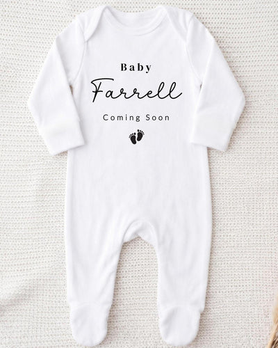A white bodysuit with the text "Baby Farrell Coming Soon" printed on it.
