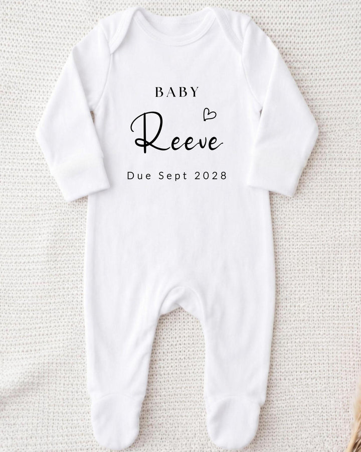 Personalisable white Baby Grow with black 'Baby Reeve Due Sept 2028' script and serif lettering with an outlined heart above the surname.