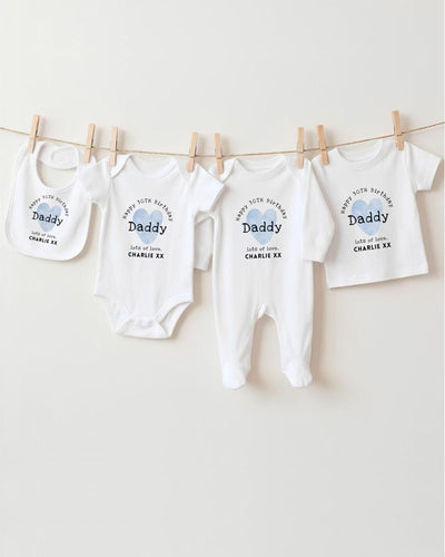 A row of white baby clothes, including onesies and bibs, hanging on a clothesline.