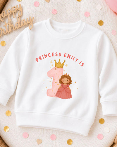 A white sweatshirt with a pink princess and the number 1 printed on it, along with the text "PRINCESS EMILY IS" and a crown.