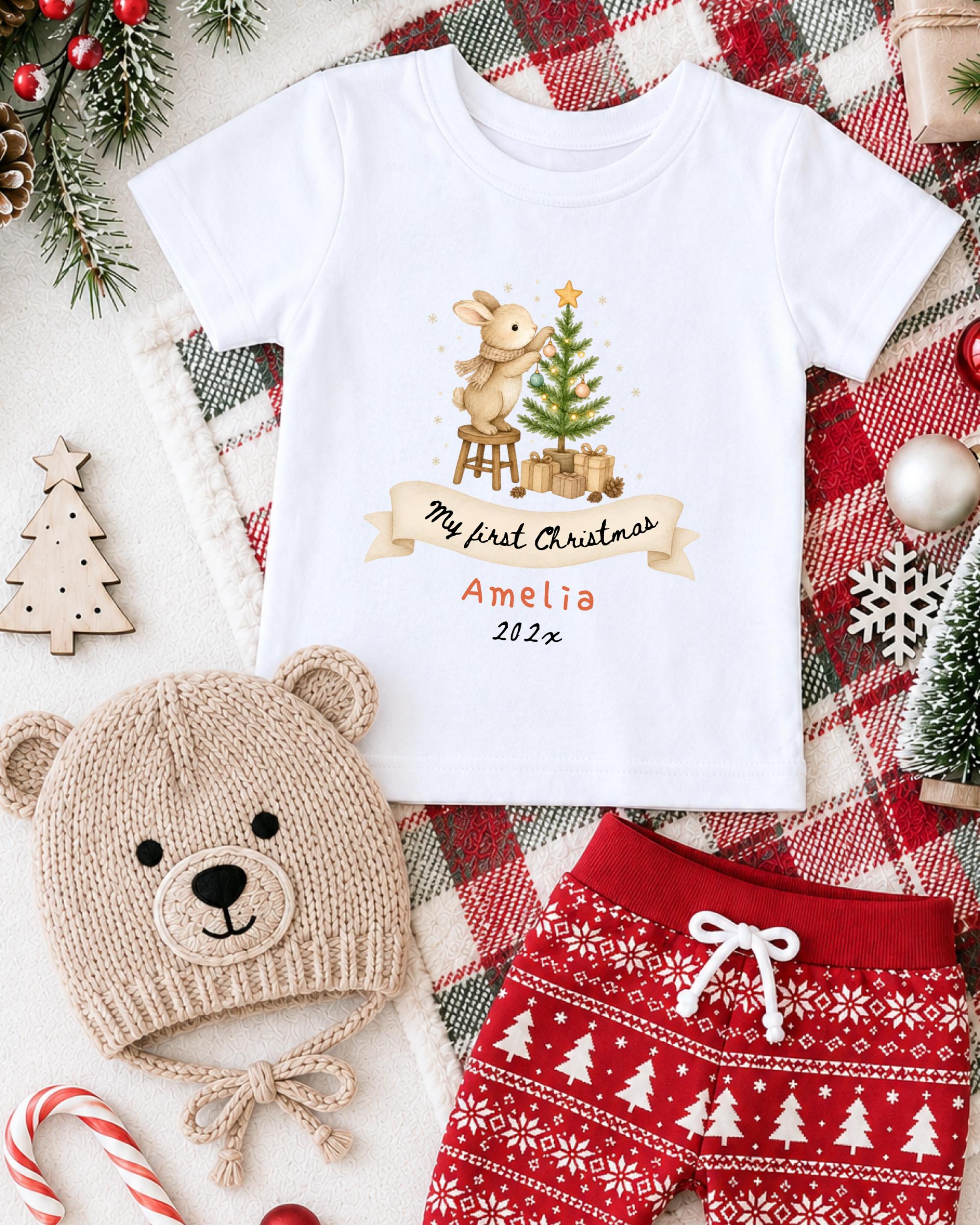 A white t-shirt with a Christmas-themed design, a beige knit hat, red shorts, and other Christmas-themed items are arranged on a plaid blanket.