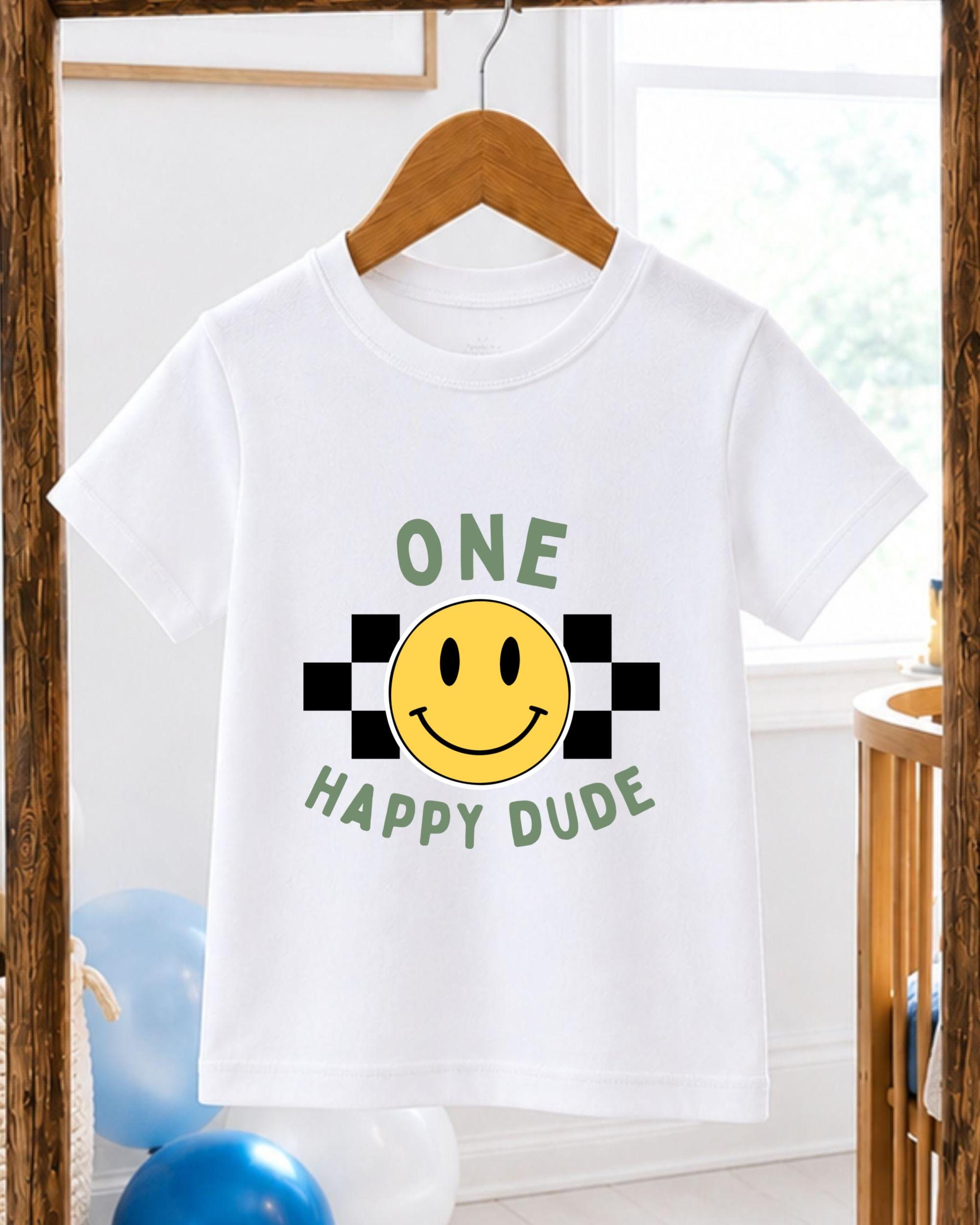 A white t-shirt with a cheerful smiley face and the text "ONE HAPPY Dude" printed on it, hanging on a wooden hanger.