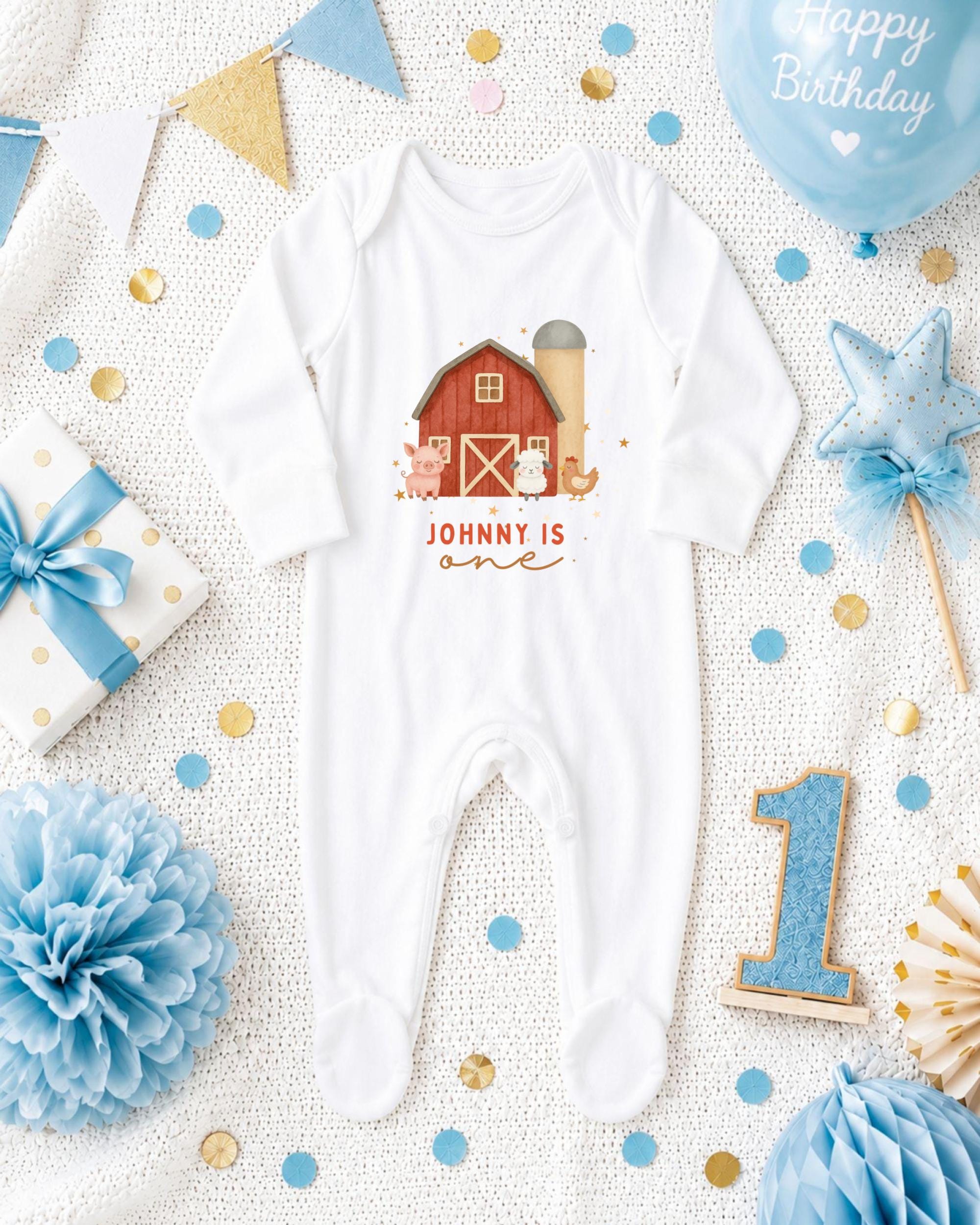 A baby onesie with a farm scene design, surrounded by birthday decorations and confetti.