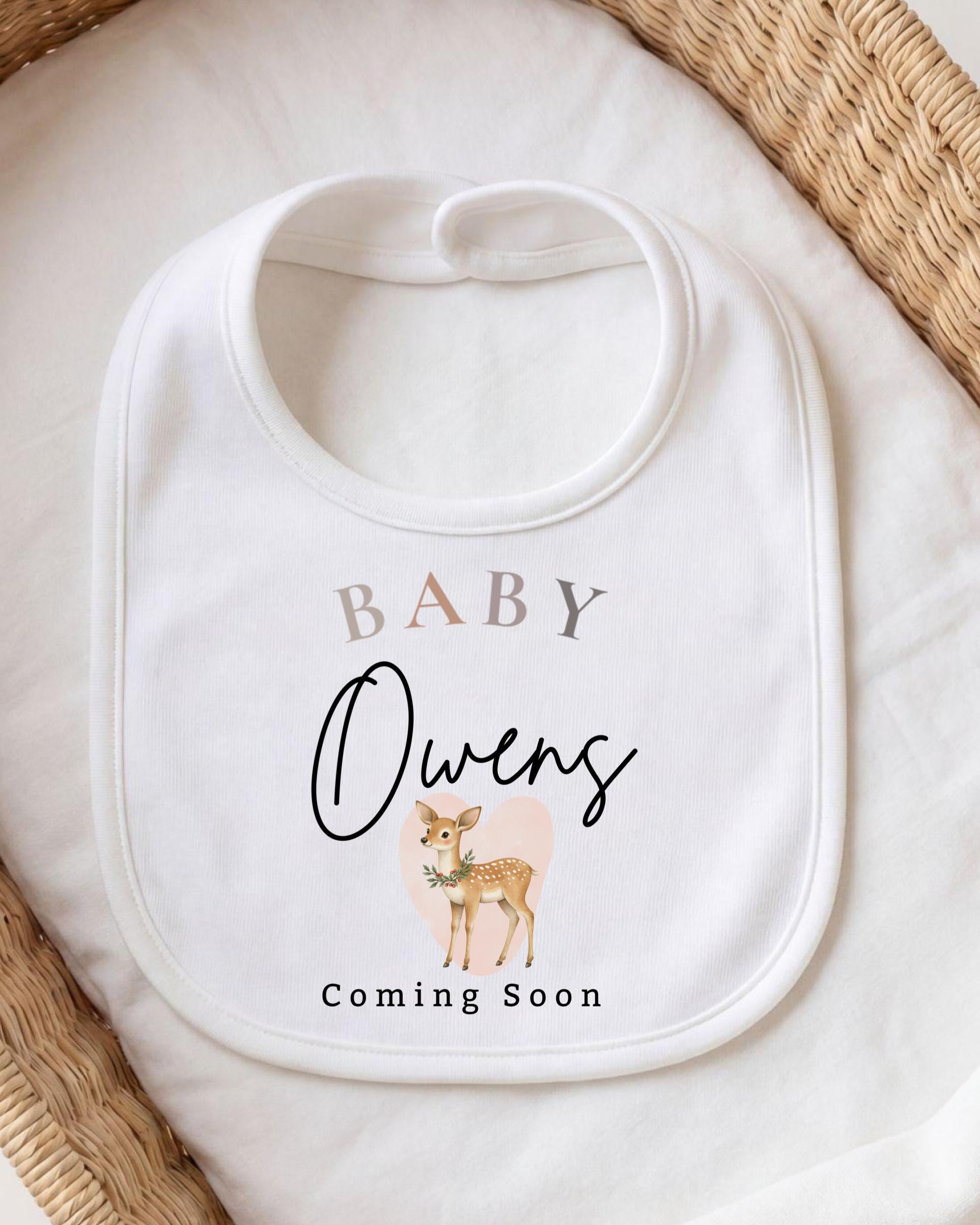 A white baby bib with a printed design of a deer and the text "BABY Owens Coming Soon".