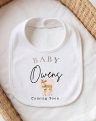 A white baby bib with a printed design of a deer and the text "BABY Owens Coming Soon".