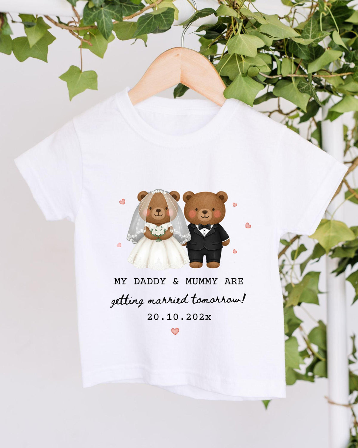 A white t-shirt with a graphic design of two teddy bears dressed as a bride and groom, along with the text "My Daddy & Mummy are getting married tomorrow!" and the date "20.10.2023".