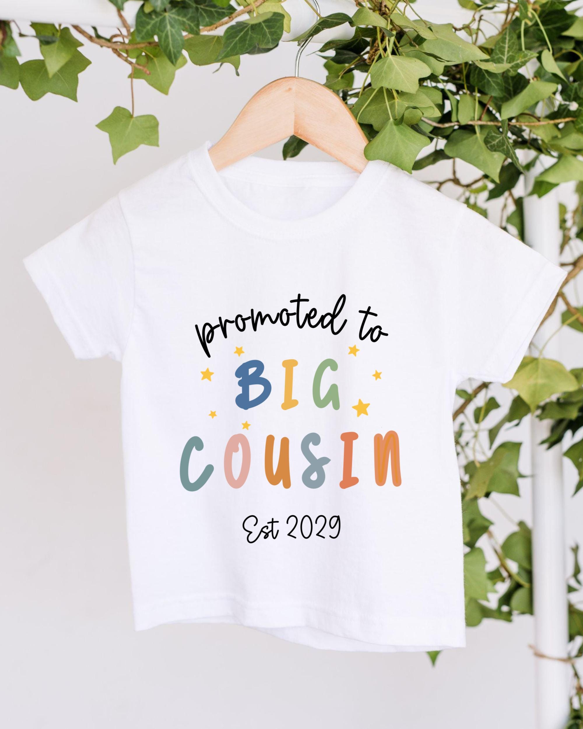 A white t-shirt with text printed on it, hanging on a wooden hanger.
