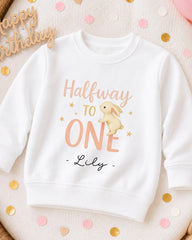 A white sweatshirt with a cartoon rabbit and the text "Halfway to One" printed on it, along with the name "Lily" below the rabbit.