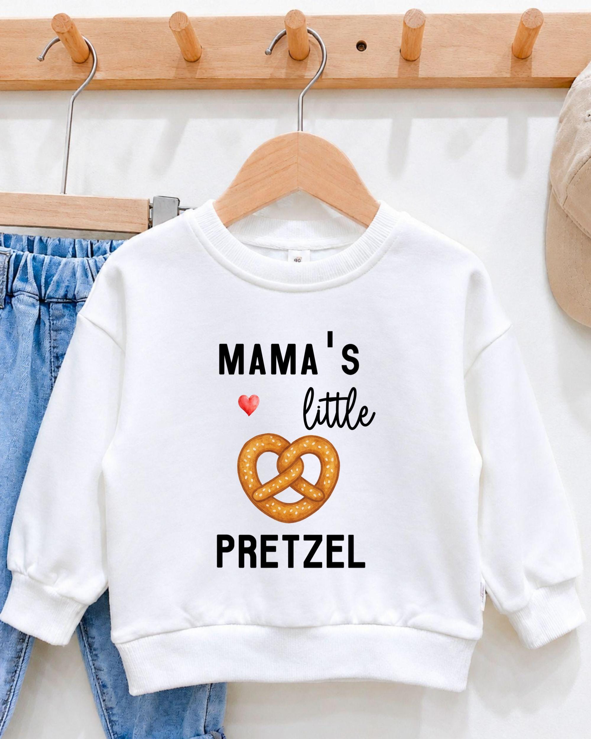 A white sweatshirt with a graphic design and text printed on it, hanging on a wooden hanger.
