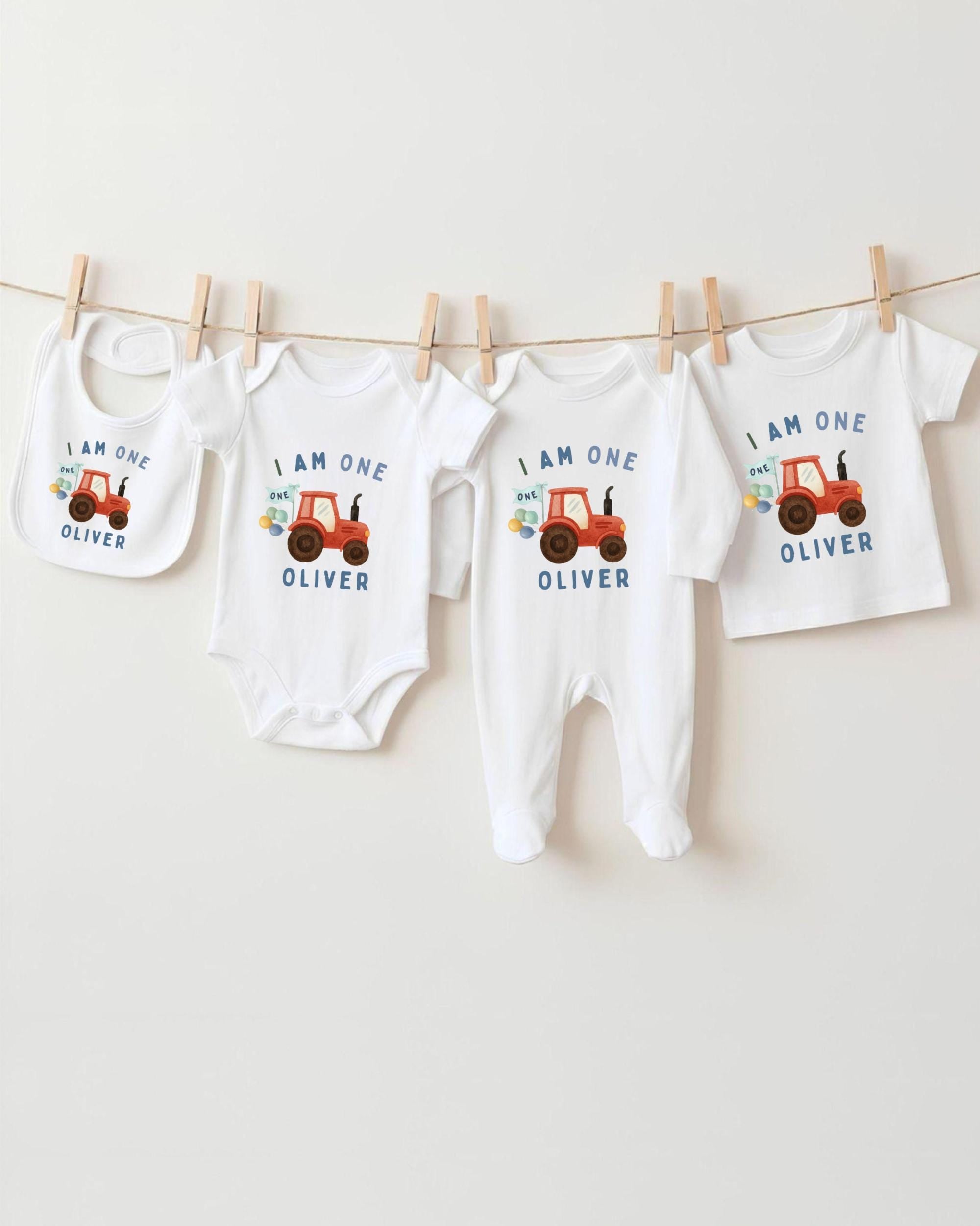 A collection of white baby clothes and bibs with the same design, featuring an orange tractor on the front, hanging on a clothesline.