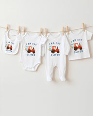 A collection of white baby clothes and bibs with the same design, featuring an orange tractor on the front, hanging on a clothesline.